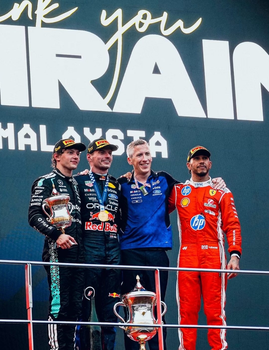 Antonelli, Verstappen, a Red Bull team member and Hamilton on the Sepang podium under a 